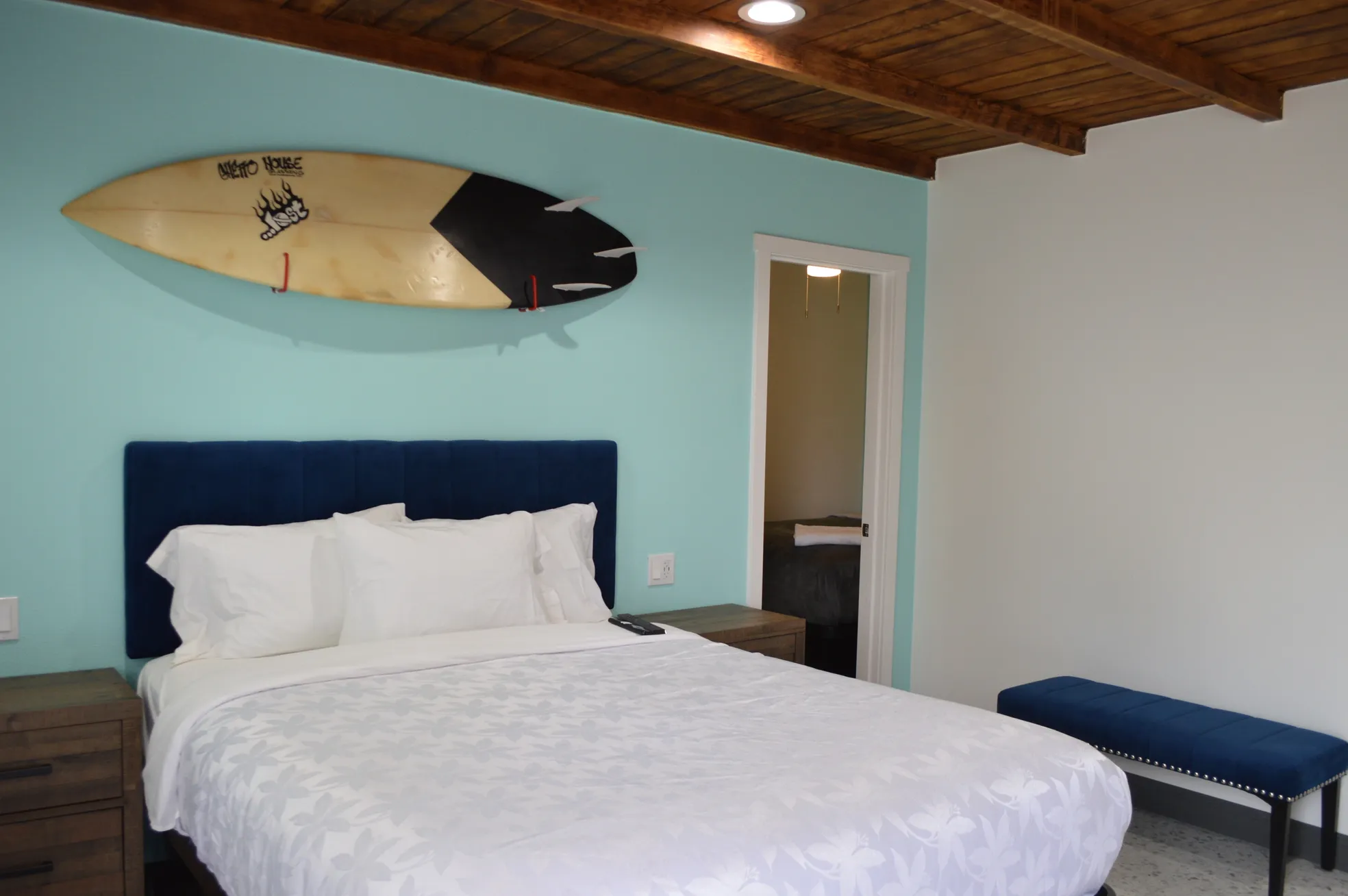Deluxe multiple-beds room with a turquoise accent wall, a surfboard mounted above the bed and a second bed visible through the doorway