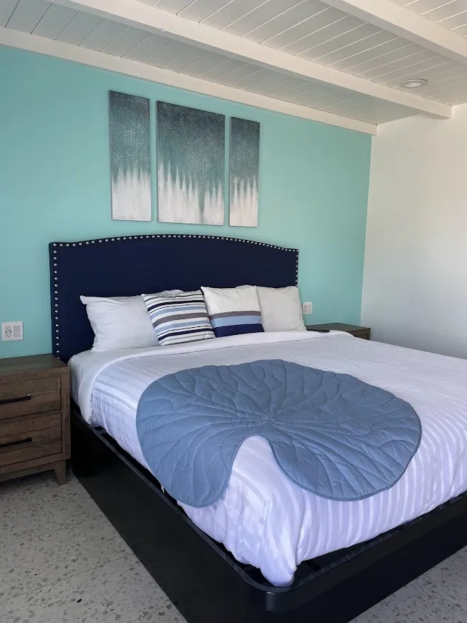 Deluxe room bed with a navy headboard trimmed in silver studs and a three-panel turquoise wall art set above it