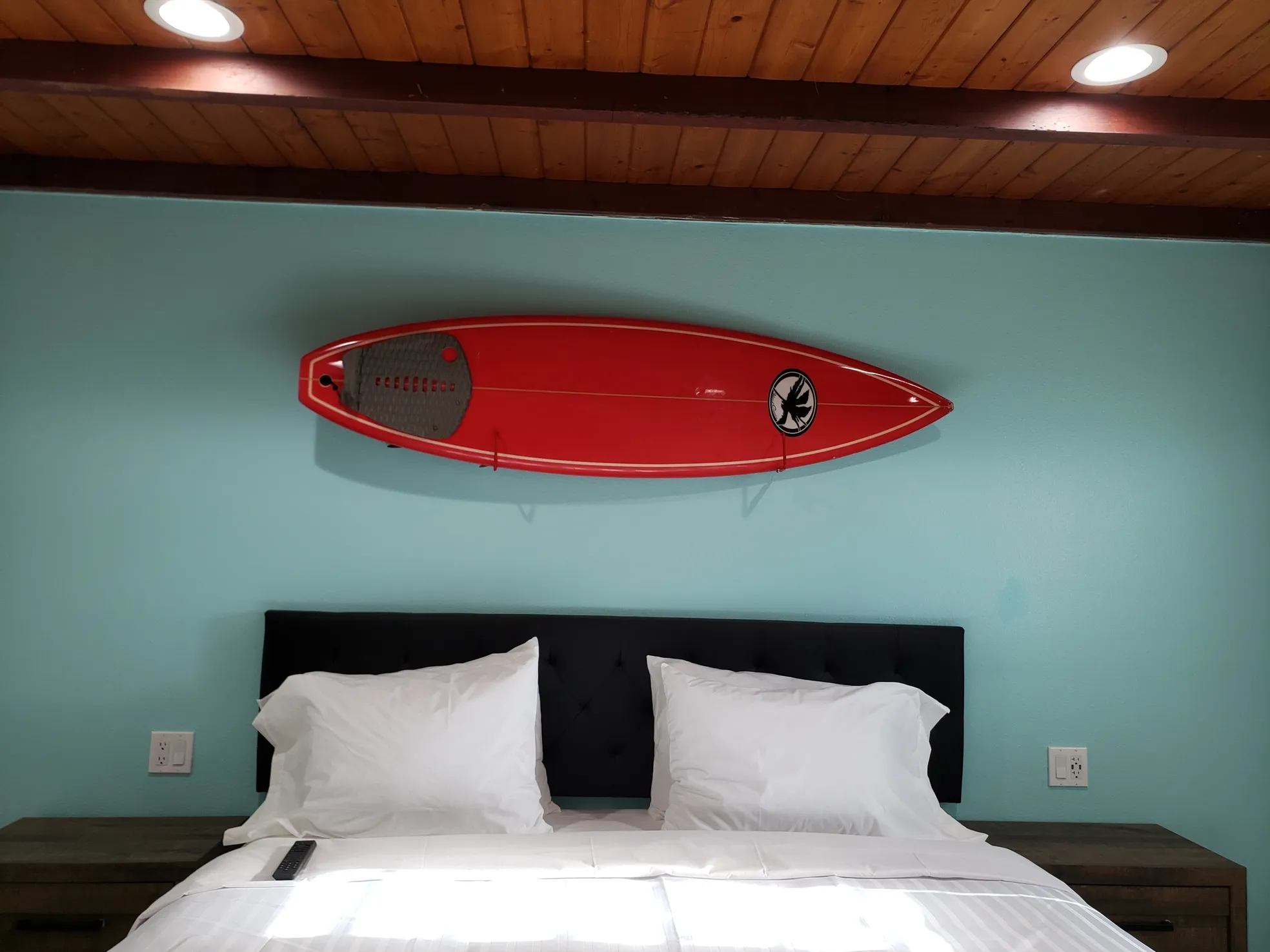Accessible room with a turquoise accent wall, a red surfboard mounted above the bed and a sloped wood-plank ceiling